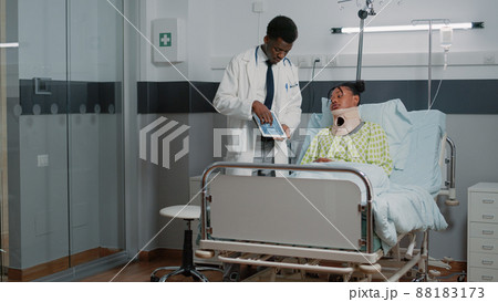 Specialist explaining radiography to woman with neck collar in hospital ward bed. Medical physician showing x ray diagnosis to injured patient wearing cervical foam. Healthcare exam Specialist explaining radiography to woman with neck collar in hospital ward bed. Medical physician showing x ray diagnosis to injured patient wearing cervical foam. Healthcare exam 88183173