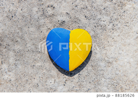 Stone in shape of a heart painted with the Ukrainian flag lies on the ground or concrete. No war. Stop the war, the genocide of Ukrainians. Flat lay with copy space. Save Ukraine people from invasion. 88185626