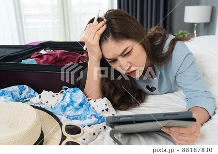 stressed woman using tablet and packing a suitcase on bed at home, holiday travel concept stressed woman using tablet and packing a suitcase on bed at home, holiday travel concept 88187830