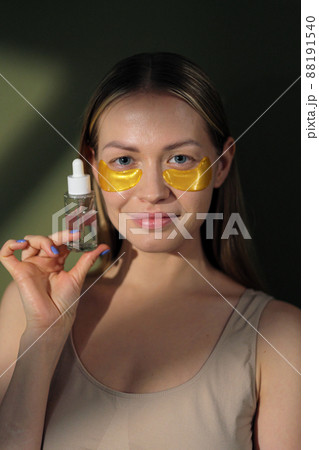 Close-up of a beautiful young caucasian blonde woman with silicone undeeye patches on her face. A woman holds a bottle with a micellar water in hands. Close-up of a beautiful young caucasian blonde woman with silicone undeeye patches on her face. A woman holds a bottle with a micellar water in hands. 88191540