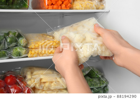 Woman putting plastic bag with cauliflower in refrigerator with frozen vegetables, closeup 88194290