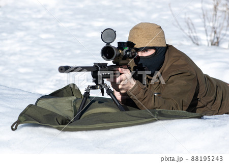 A sniper rifles with an optical sight in hands man aiming laying on snow winter day l A sniper rifles with an optical sight in hands man aiming laying on snow winter day l 88195243