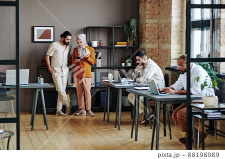 Two young Muslim employees in casualwear discussing data in mobile phone Two young Muslim employees in casualwear discussing data in mobile phone 88198089