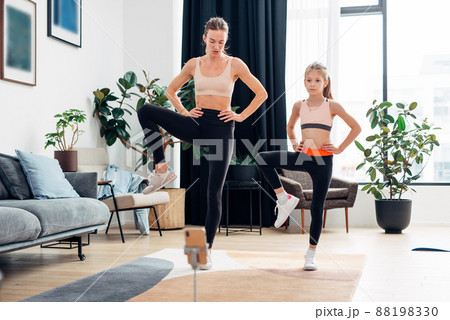 Home training. Mother and daughter warming up, stretching leg muscles Home training. Mother and daughter warming up, stretching leg muscles 88198330