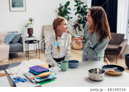 Mother braids her daughters plaits before school at the kitchen table 88198356