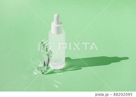 Serum skincare product with collagen and peptide in white bottle with dropper on green backdrop with crystal glass prism refracting light effects and rays of light. Product mockup packaging 88202095