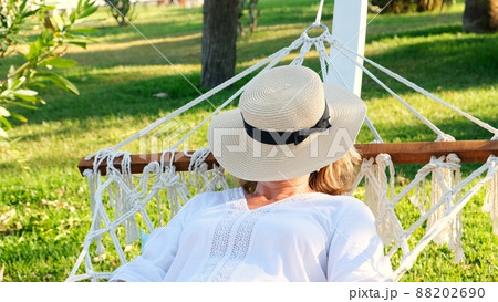 female age 50-60 in a straw hat is resting in a hammock around the palm trees and enjoying the female age 50-60 in a straw hat is resting in a hammock around the palm trees and enjoying the 88202690