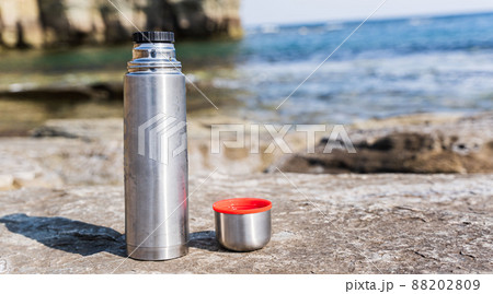 Thermos and mug on stone on the beach at sunset near the sea 88202809