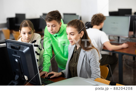 Female teacher and teen students looking at monitor screen during lesson 88204208