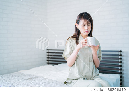ベッドで飲み物を飲むミドル世代の女性(困る) ベッドで飲み物を飲むミドル世代の女性(困る) 88206850