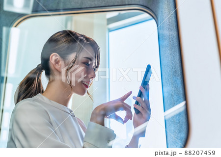 フリーアドレスオフィスの防音電話ボックスで電話をする女性 フリーアドレスオフィスの防音電話ボックスで電話をする女性 88207459