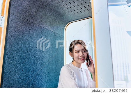 フリーアドレスオフィスの防音電話ボックスで電話をする女性 フリーアドレスオフィスの防音電話ボックスで電話をする女性 88207465