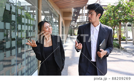 Two happy business colleagues talking to each other while walking outside modern office building. Two happy business colleagues talking to each other while walking outside modern office building. 88209269