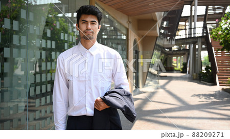 Elegant young businessman standing outside modern office building and looking confidently at camera. Elegant young businessman standing outside modern office building and looking confidently at camera. 88209271