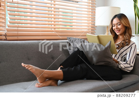 Pretty woman reading a book on sofa while spending leisure time at home. 88209277