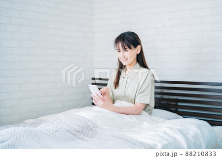 ベッドでスマホを使うミドル世代の女性（笑顔） 88210833