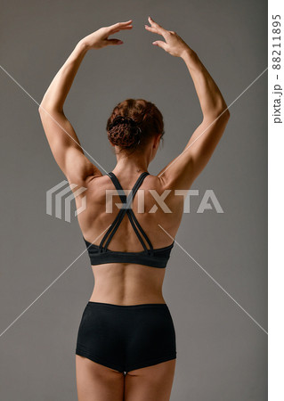 Back view of slim gymnast or ballerina in black leotard dancing on a gray studio background Back view of slim gymnast or ballerina in black leotard dancing on a gray studio background 88211895
