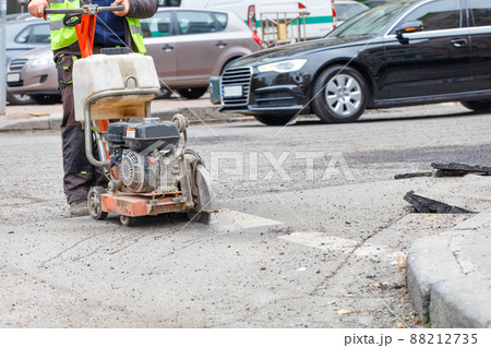 A road worker cuts with a gasoline cutter the destroyed old asphalt on the roadway for the subsequent repair of the road surface. A road worker cuts with a gasoline cutter the destroyed old asphalt on the roadway for the subsequent repair of the road surface. 88212735