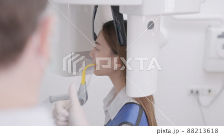 On a panoramic x-ray machine, the dentist aligns the bite of a woman. In a dental clinic, a woman dressed in a lead apron stands still as a panoramic X-ray machine circles her head.. 88213618