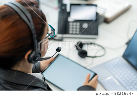 Rear view of a woman in a headset using a digital tablet while sitting at a desk. Friendly female support service operator at work. 88216547