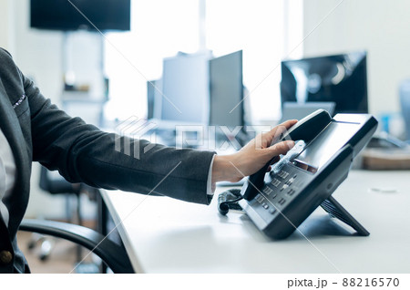 Close-up of a female employee's hand on a landline phone. Woman picks up a push-button telephone at the workplace in the office 88216570