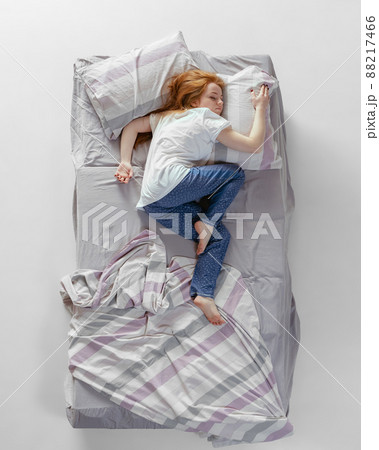 Aerial view of red-headed young sleeping girl in cotton homewear lying in huge gray bed. Concept of health, home interior, relax time, family, dreams 88217466