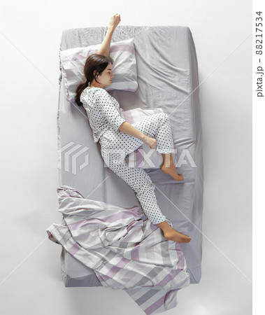 Aerial view young sleeping girl in white pajamas lying in big gray bed. Concept of health, home interior, relax time, family, dreams Aerial view young sleeping girl in white pajamas lying in big gray bed. Concept of health, home interior, relax time, family, dreams 88217534
