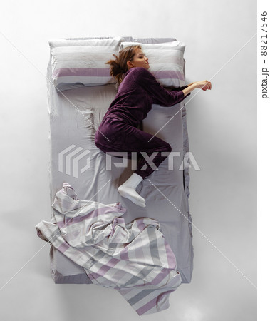 Creative portrait of young girl wearing wine color homewear, pajamas sleeping in big bed. Concept of health, home interior, relax time, family, dreams Creative portrait of young girl wearing wine color homewear, pajamas sleeping in big bed. Concept of health, home interior, relax time, family, dreams 88217546