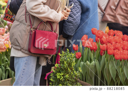 Abstract girl with smartphone in her hands and bright red handbag admires red tulips. Women fashion accessories concept 88218085