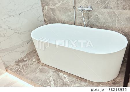 Luxury big oval bathtub in bathroom with black and white marble tiles on walls and floor. Luxury big oval bathtub in bathroom with black and white marble tiles on walls and floor. 88218936