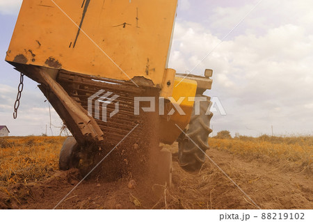 A tractor plows a row of potatoes, harvesting yellow potatoes in the village in the field. A tractor plows a row of potatoes, harvesting yellow potatoes in the village in the field. 88219102
