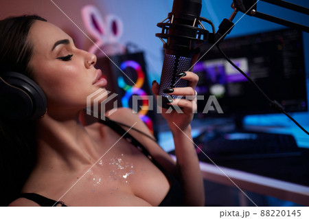 Happy woman putting on headphones and playing computer game. Female gamer in glasses sitting and looking at computer monitor. Happy woman putting on headphones and playing computer game. Female gamer in glasses sitting and looking at computer monitor. 88220145