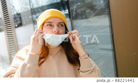 Happy smiling Woman taking off mask outdoor. Coronavirus ended. We are safe. Cheerful young woman in yellow hat removing protective mask off her face. Happy smiling Woman taking off mask outdoor. Coronavirus ended. We are safe. Cheerful young woman in yellow hat removing protective mask off her face. 88221441