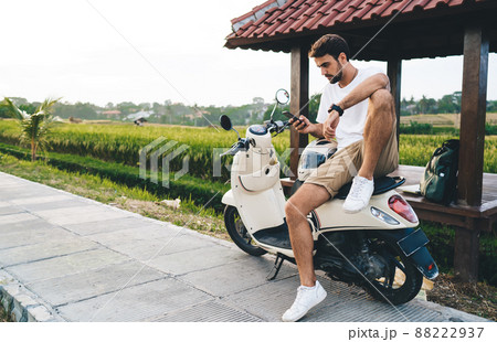 Focused young biker using smartphone on scooter in countryside Focused young biker using smartphone on scooter in countryside 88222937