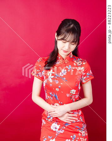Portrait of a young asian woman in traditional cheongsam qipao dress having a stomach ache isolated over red background. Portrait of a young asian woman in traditional cheongsam qipao dress having a stomach ache isolated over red background. 88223223