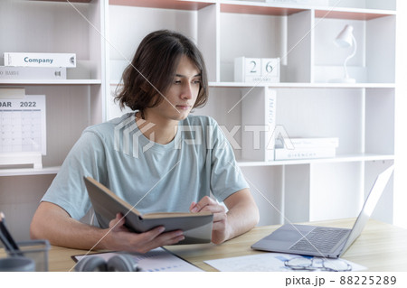 Asian man taking notes in notebook while studying online in laptop at home, Video chat, Online communication , Stay home, New normal, Distance learning , Social distancing, Learn online. Asian man taking notes in notebook while studying online in laptop at home, Video chat, Online communication , Stay home, New normal, Distance learning , Social distancing, Learn online. 88225289