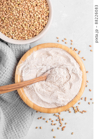 Buckwheat flour in a wooden bowl with wooden spoon and raw green buckwheat grain in a bowl on grey stone background Buckwheat flour in a wooden bowl with wooden spoon and raw green buckwheat grain in a bowl on grey stone background 88226083