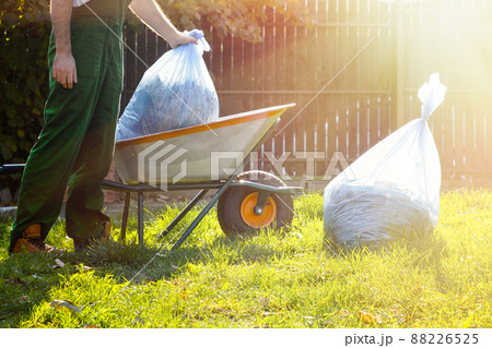 close-up of a man in a green uniform collecting garbage bags in a cart at sunset close-up of a man in a green uniform collecting garbage bags in a cart at sunset 88226525