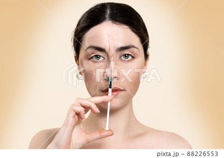 Portrait of a beautiful woman holding a syringe with an injection near the face, divided into two parts-young and old.Result before and after the procedures. Beige background. Concept of rejuvenation 88226553