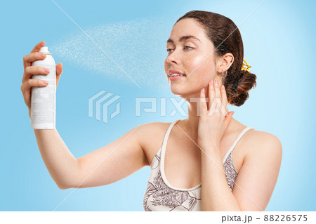 A young Caucasian woman with wet skin splashes thermal water on her face. Blue background. Concept of cosmetology, skin care and moisturizing A young Caucasian woman with wet skin splashes thermal water on her face. Blue background. Concept of cosmetology, skin care and moisturizing 88226575