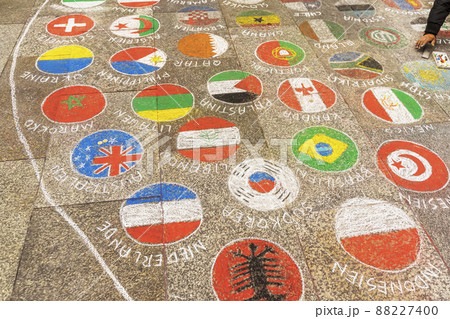 Hand of teenager drawing multi-colored flags of different countries in circles on pavement with multi-colored crayons 88227400