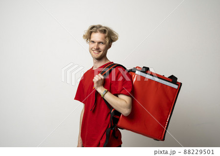 Delivery man employee man in a red tshirt uniform workwear work as a dealer courier and hold red thermal food bag backpack isolated on white background. Service concept. 88229501