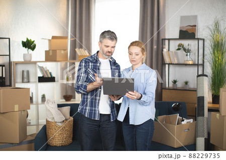 Mature man and his pretty wife using laptop while relocating to new flat Mature man and his pretty wife using laptop while relocating to new flat 88229735
