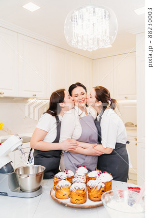 mother and daughters with Kraffins, easter cakes and Panettones in the kitchen. mother and daughters with Kraffins, easter cakes and Panettones in the kitchen. 88230003