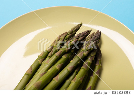 High angle close-up view of asparagus vegetables in white plate against blue background High angle close-up view of asparagus vegetables in white plate against blue background 88232898
