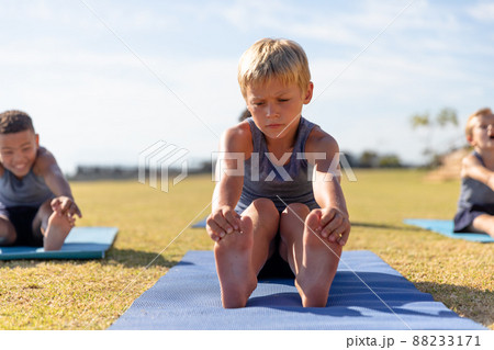 Multiracial elementary schoolboys touching toes while exercising on yoga mat in school ground Multiracial elementary schoolboys touching toes while exercising on yoga mat in school ground 88233171