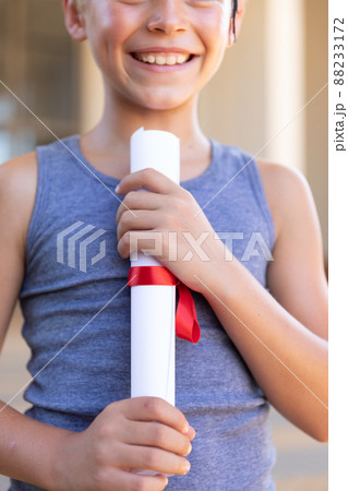 Midsection of smiling caucasian elementary schoolboy holding degree certificate Midsection of smiling caucasian elementary schoolboy holding degree certificate 88233172