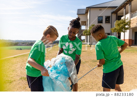 Multiracial elementary schoolboys collecting plastic in garbage bag while standing school ground Multiracial elementary schoolboys collecting plastic in garbage bag while standing school ground 88233180