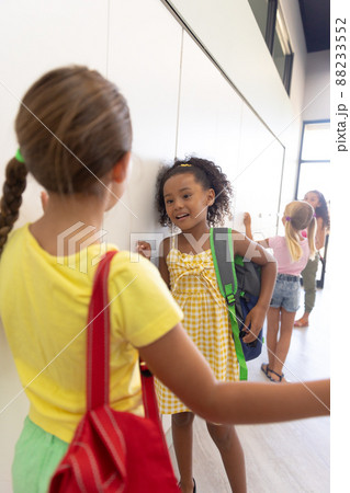 Multiracial elementary schoolgirls talking while standing by lockers in school corridor Multiracial elementary schoolgirls talking while standing by lockers in school corridor 88233552