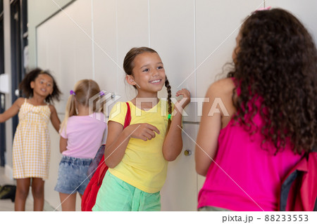 Multiracial elementary schoolgirls talking while standing by lockers in school corridor Multiracial elementary schoolgirls talking while standing by lockers in school corridor 88233553